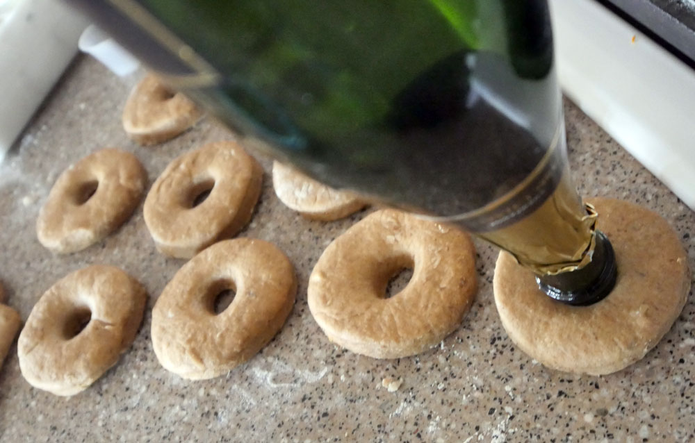cutting centers out of dough donuts with a champagne bottle