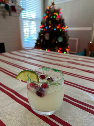 mojito with lime and cranberry garnish in front of Christmas tree